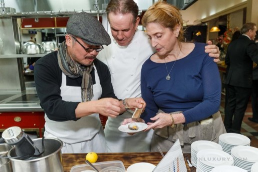 Chef and two women tasting food in a professional kitchen setting.