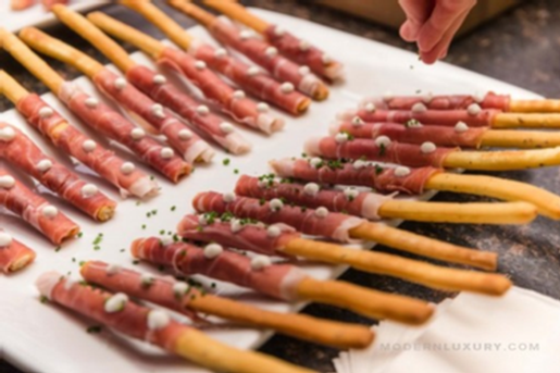 Gourmet appetizer skewers with prosciutto, cheese, and herbs on a white platter.