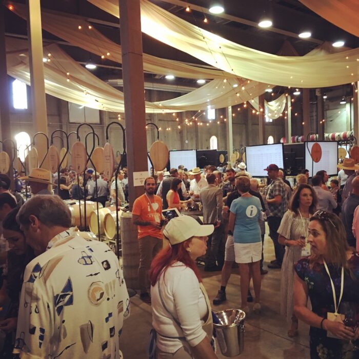 Crowd at the 90 Plus Wine Club event during Auction Napa Valley 2018 with wine tasting booths and elegant decor.